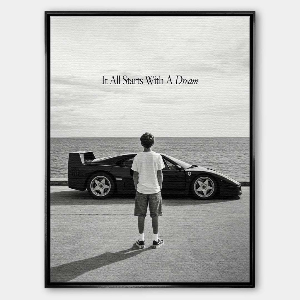 Czarno-biały obraz na płótnie przedstawiający chłopca patrzącego na sportowe auto i morze. Wydruk galeryjny z motywacyjnym napisem It All Starts With A Dream.