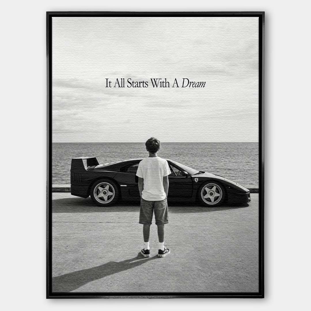 Czarno-biały obraz na płótnie przedstawiający chłopca patrzącego na sportowe auto i morze. Wydruk galeryjny z motywacyjnym napisem It All Starts With A Dream.