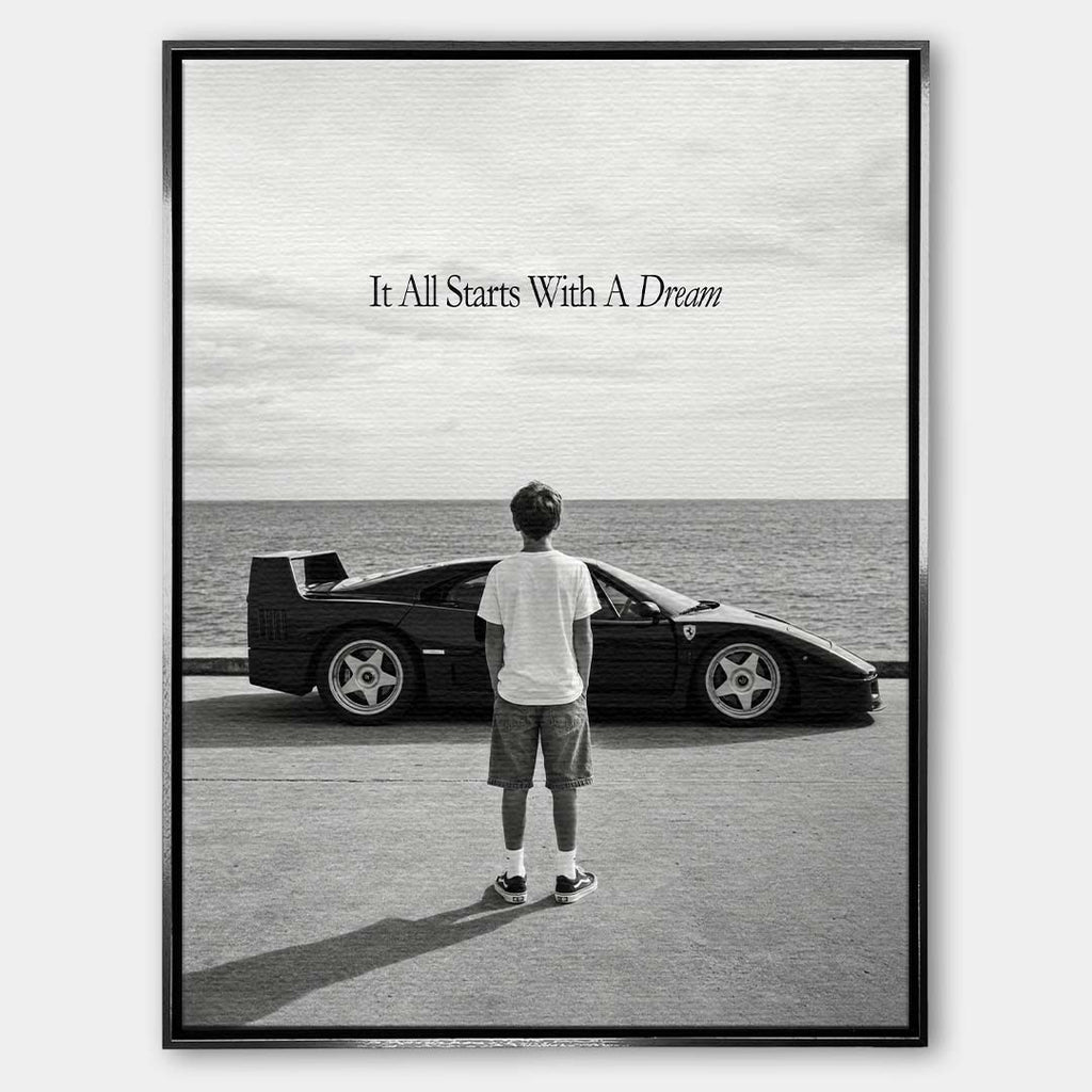 Czarno-biały obraz na płótnie przedstawiający chłopca patrzącego na sportowe auto i morze. Wydruk galeryjny z motywacyjnym napisem It All Starts With A Dream.