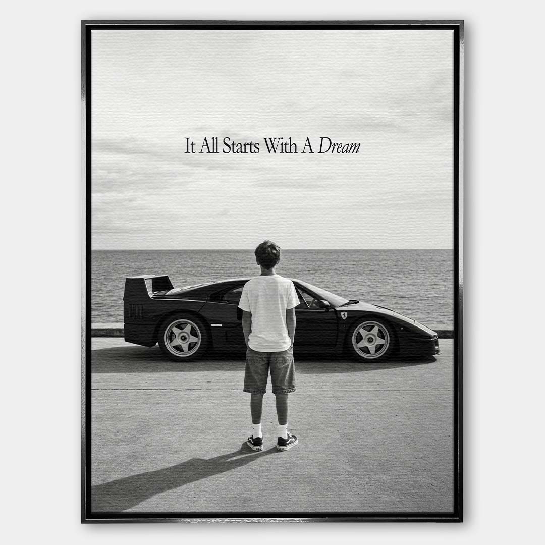 Czarno-biały obraz na płótnie przedstawiający chłopca patrzącego na sportowe auto i morze. Wydruk galeryjny z motywacyjnym napisem It All Starts With A Dream.