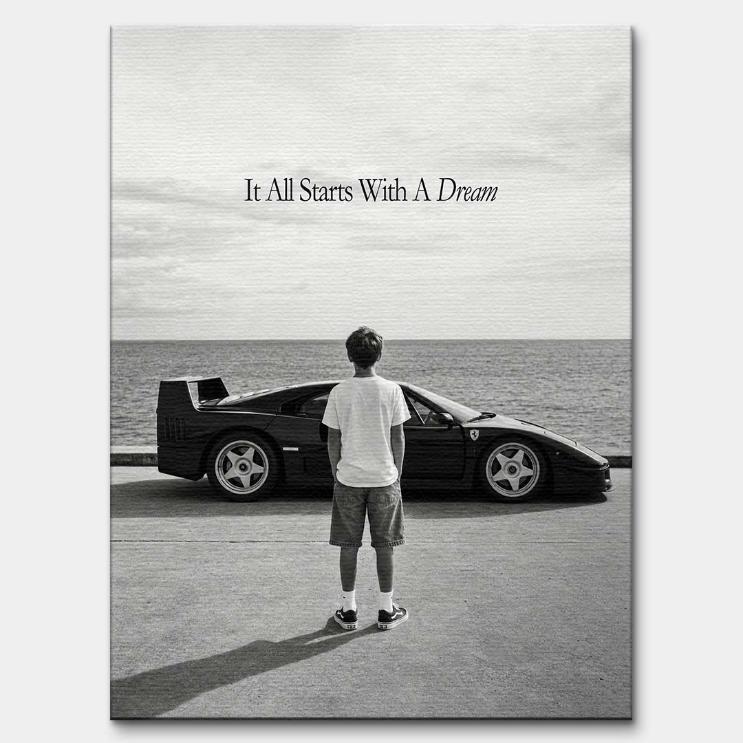 Czarno-biały obraz na płótnie przedstawiający chłopca patrzącego na sportowe auto i morze. Wydruk galeryjny z motywacyjnym napisem It All Starts With A Dream.