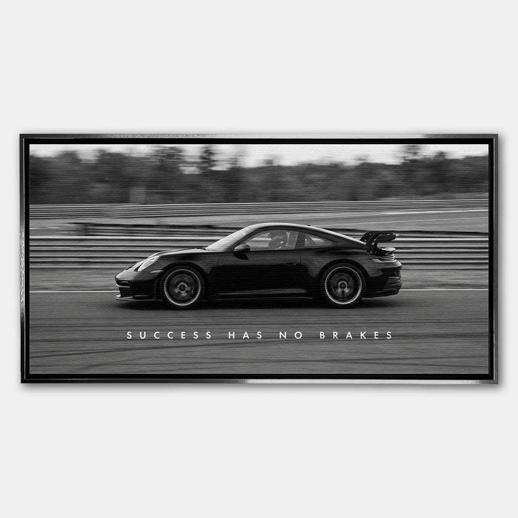 Czarno-biały obraz na płótnie przedstawiający Porsche 911 w szybkim ruchu na torze z napisem Success Has No Brakes. Motywacyjna sztuka ścienna do biura.