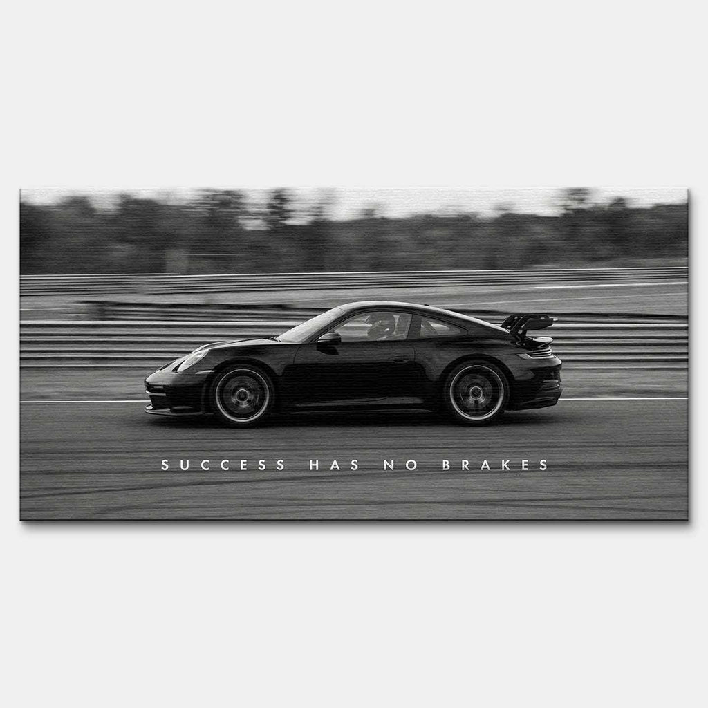 Czarno-biały obraz na płótnie przedstawiający Porsche 911 w szybkim ruchu na torze z napisem Success Has No Brakes. Motywacyjna sztuka ścienna do biura.