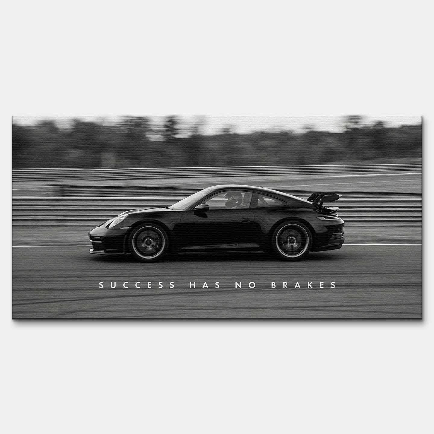 Czarno-biały obraz na płótnie przedstawiający Porsche 911 w szybkim ruchu na torze z napisem Success Has No Brakes. Motywacyjna sztuka ścienna do biura.