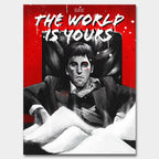 Obraz na płótnie przedstawiający Tony'ego Montanę z filmu „Scarface”, siedzącego na czarnym fotelu na tle czerwonego tła z białym napisem „The World Is Yours”; intensywna scena w czarno-białej kolorystyce z kontrastującymi elementami czerwieni i bieli.